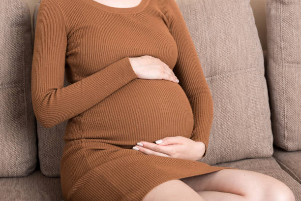 istock Pregnant Lady Having Massaging Lower belly Sitting On Sofa Indoor. Pregnancy Problems Concept. Maternity healthcare 1318591011