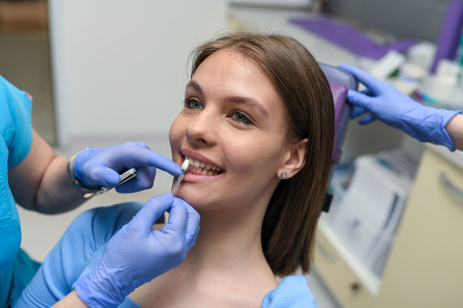 The dentist compares the dental veneer with the patient's teeth.