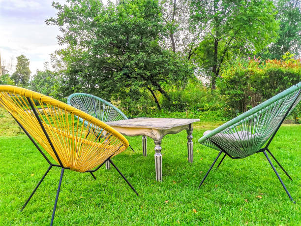 Yellow wicker egg chairs and table on green lawn in summer garden