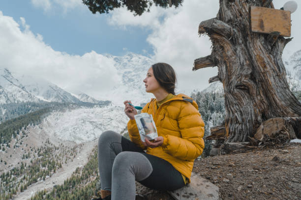 Woman eating dried meal near  Nanga Parbat Young Caucasian eating dried meal  and looking at Nanga Parbat mountain in Pakistan from balcony base camp stock pictures, royalty-free photos & images