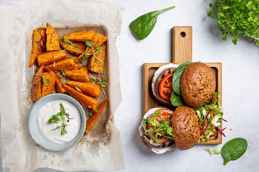 Meat free plant based burgers served with sweet potato wedges, green mix salad and white sauce on gray table. Healthy vegan or vegetarian food concept. Top view.