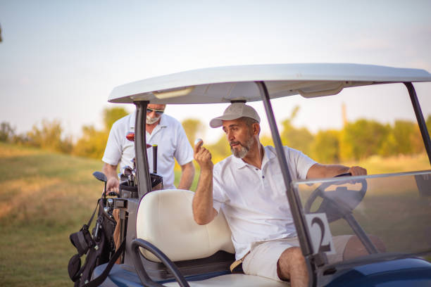 コート上の2人の先輩ゴルファー。ゴルフカートに座っている男。 コート上の2人の先輩ゴルファー。 - golf cart golf bag horizontal outdoors ストックフォトと画像