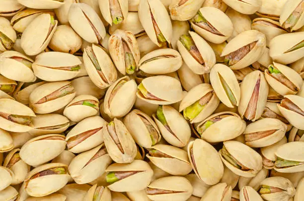 Roasted and salted pistachio seeds with shell, background, from above. Snack food, made from fruits of Pistacia vera. Green kernels in light yellow shells, ready to eat. Backdrop. Macro food photo.