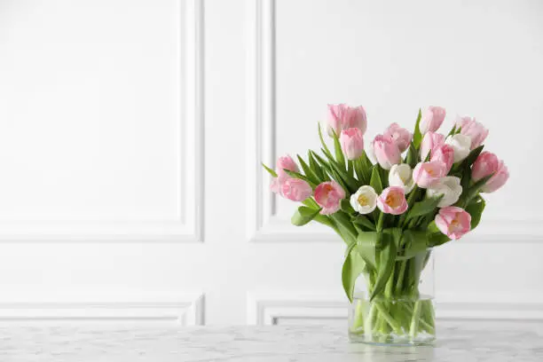 Photo of Beautiful bouquet of tulips in glass vase on white marble table. Space for text
