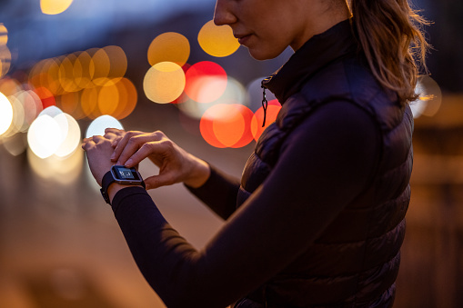 Cropped shot of a woman monitoring fitness process on smartwatch after a workout at night. Woman using a fitness app on her smartwatch. She is outdoors in the city at night for a run.