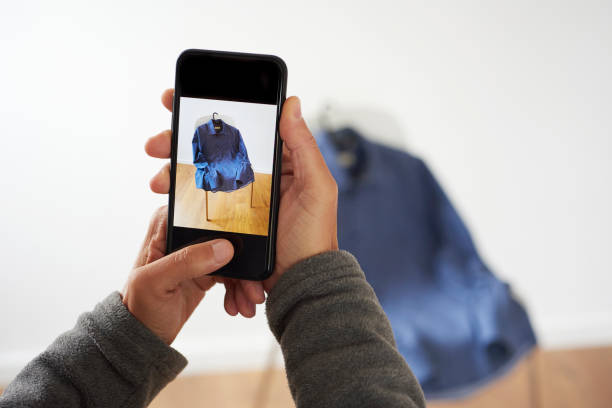 man sells a shirt on an online marketplace app closeup of a young caucasian man taking a picture, with his smartphone, of a shirt to sell it on an online marketplace app to sell and buy secondhand goods clothing swap photos stock pictures, royalty-free photos & images