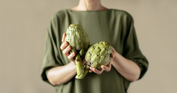 Woman holding fresh ripe artichokes in her hands, healthy vegetarian food ingredient concept