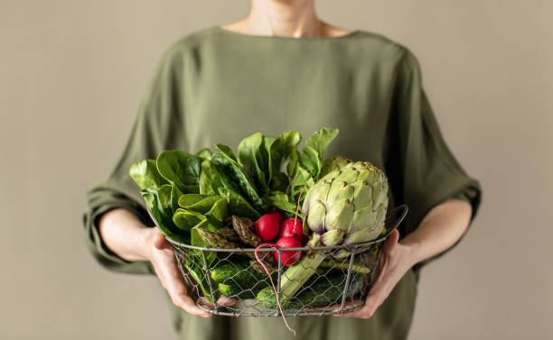 Woman holding a basket full of fresh veggie produce, healthy food concept stock photo