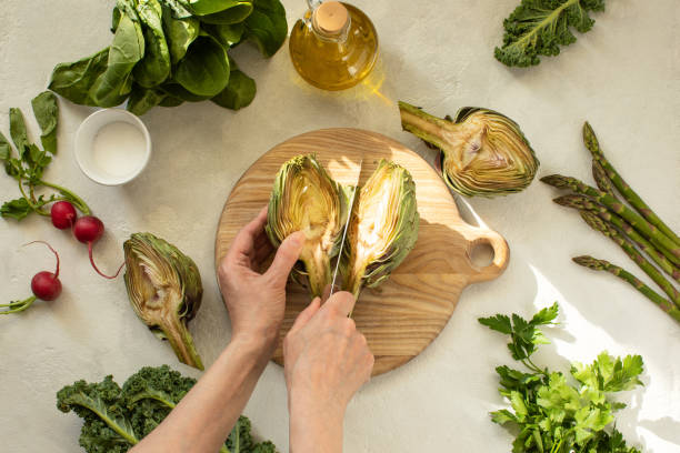 Local season ingredients culinary concept Season ingredients culinary concept, a woman is cutting fresh harvest artichoke during a sunny spring day, top-down view artichoke diet stock pictures, royalty-free photos & images