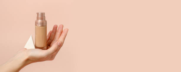 istock Applying foundation on makeup sponge. Woman's hands with neutral manicure holding bottle of concealer or toner foundation, cream and beauty blender, make up artist background, banner, flyer 1318602131