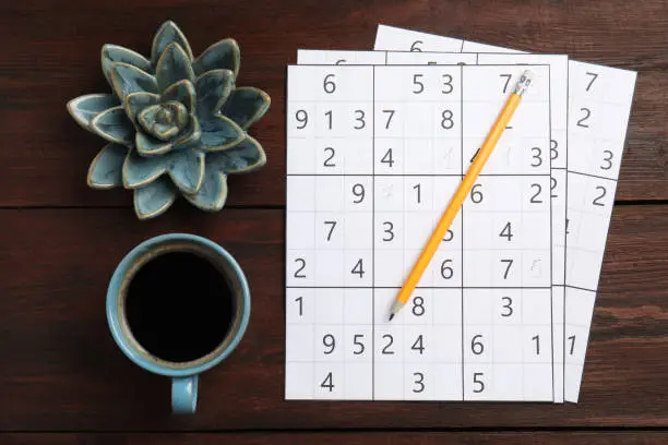 Photo of Sudoku, pencil, cup of coffee and decorative succulent on wooden table, flat lay