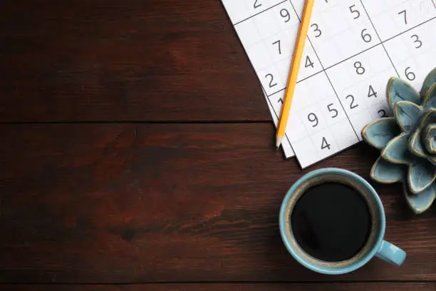 Photo of Sudoku, pencil, cup of coffee and decorative succulent on wooden table, flat lay. Space for text