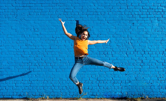 The portrait of a cheerful woman jumping with blue background.