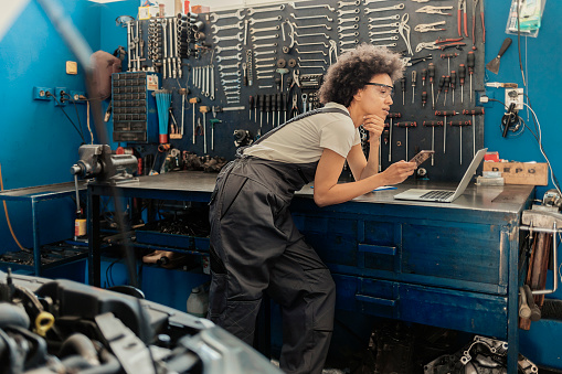 Young African American Female Auto Mechanic Using Cell Phone in a Workshop. Copy Space.