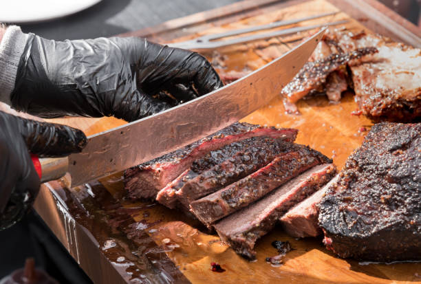 Slicing a portion of roast beef brisket with a large knife Gloved hands of a chef slicing a portion of delicious juicy tender roast beef brisket with a large knife in a close up on the blade and cutting board carving set stock pictures, royalty-free photos & images