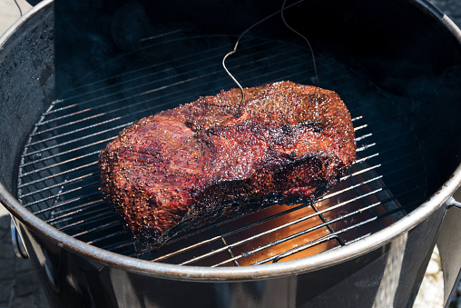 Thermometer wire in a portion of spicy lean beef brisket roasting in a metal BBQ or roasting pot in a high angle view
