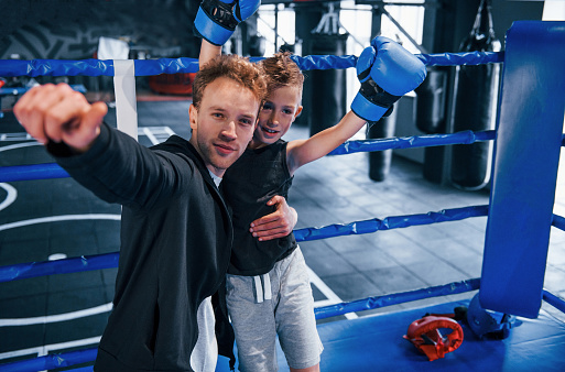 Boxing coach standing in the ring with boy and celebrating victory together.