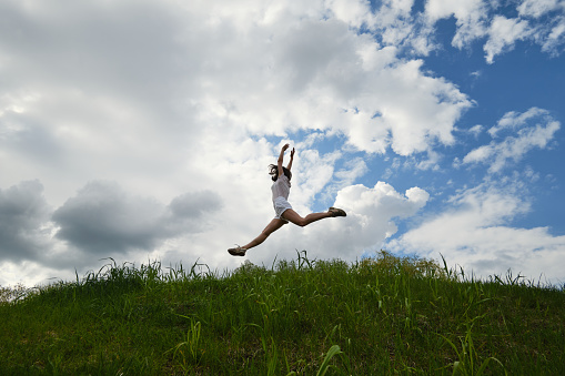 Happy girl jumping against the background of blue sky and clouds.