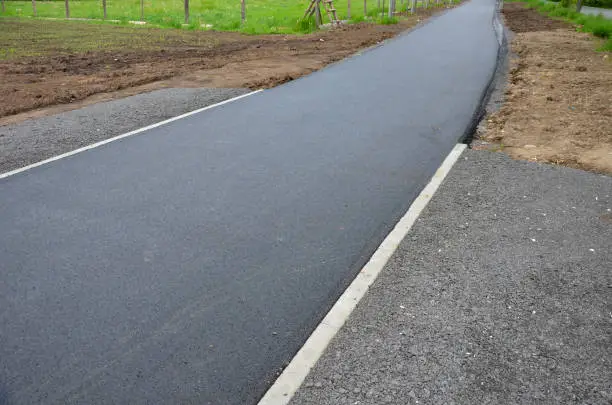 recycled asphalt crumb is used on the edge of the new cycle path and in the subsoil of the asphalt road. between the field and the path behind the curb a parking lot. bitumen, subsoil