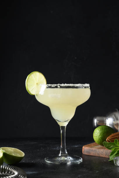 istock Classic Margarita cocktail with lime and ice cube on black background. Freshness summer alcoholic beverage. 1318616334