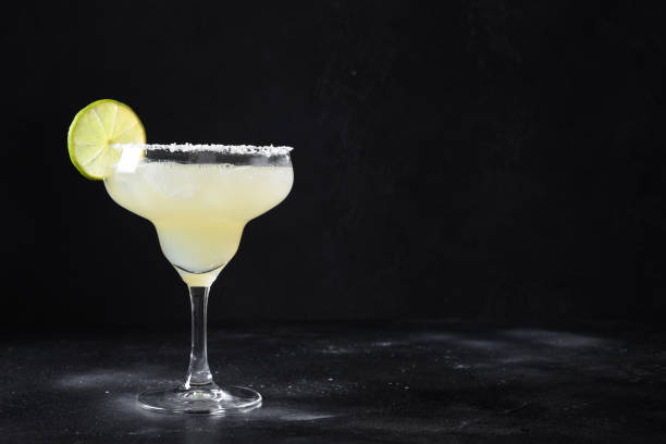 istock Classic Margarita cocktail with lime juice and ice cube on black background. 1318616336