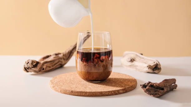 krem mleczny wlewa się do przezroczystej szklanki czarnej kawy na minimalistycznym beżowym, naturalnym drewnianym tle. - zwolnione tempo zdjęcia i obrazy z banku zdję�ć