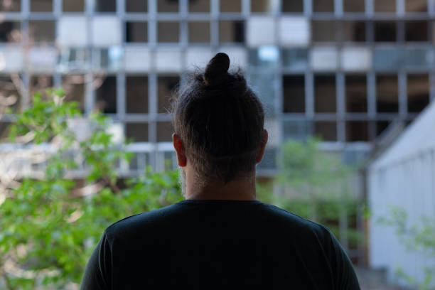 istock Man standing in front of abandoned destroyed building, his back facing camera 1318620134