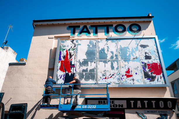 Brighton, UK - 17 May, 2021: workmen busy removing an advertisement from a billboard on the side of a tattoo parlour in Brighton, UK.