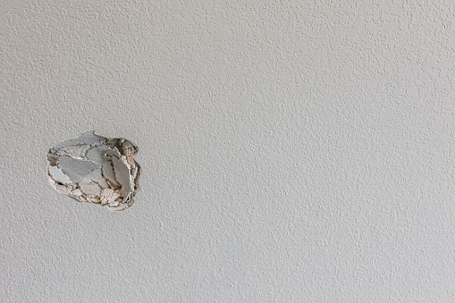 A hole in the wall of a hallways caused by a fist punching through the wall to create a large hole that needs repair.