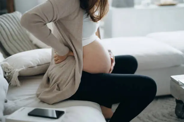 Cropped shot of Asian pregnant woman touching her belly and lower back, suffering from backache. Pregnancy health, wellbeing concept