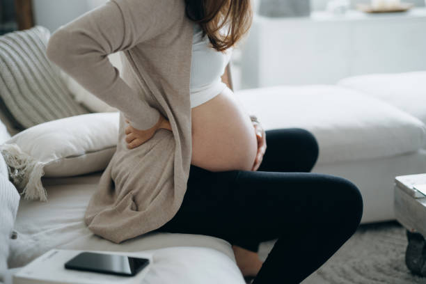 cropped shot of asian pregnant woman touching her belly and lower back, suffering from backache. pregnancy health, wellbeing concept - labour room imagens e fotografias de stock