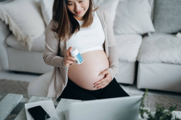 若いアジアの妊婦は、自宅でラップトップを使用して医師とビデオ通話を持っています, 手持ちの薬について相談.遠隔医療と妊娠のライフスタイル - abdomen gynecological examination women loving ストックフォトと画像