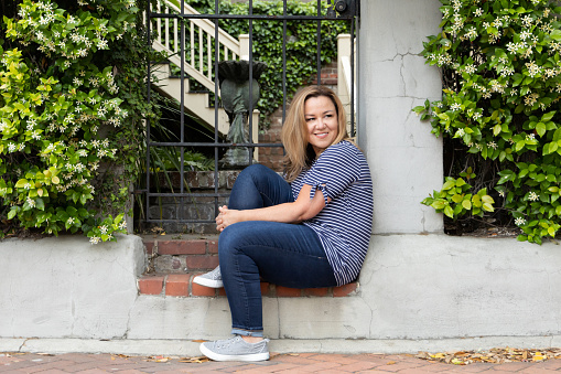 a single woman in her 40's outside in Savannah, Georgia in the spring looking away and smiling.