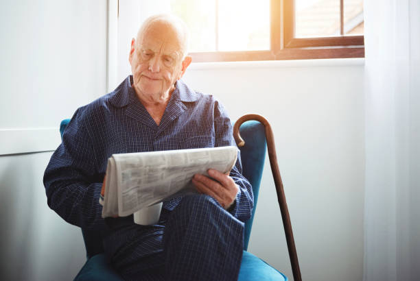 foto de un anciano sentado y leyendo un periódico en casa - reading newspaper break tea fotografías e imágenes de stock