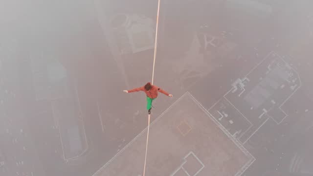 Drone shot of slackliner balances on a sling over a precipice in the fog.