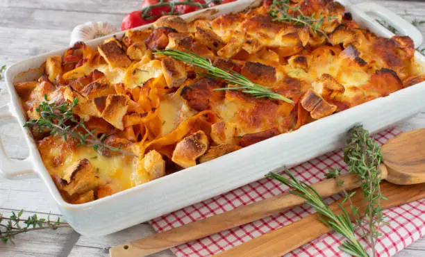 chicken Pasta casserole or gratin  with a delicious italian tomato sauce gratinated with mozzarella cheese and croutons served in baking dish on white wooden and rustic table background