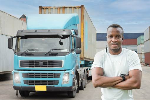 Professional truck driver Standing arm folded smiling in front of the semi truck container yard. African young man cheerful proud business owner  Delivery transportation carry Import Export Warehouse
