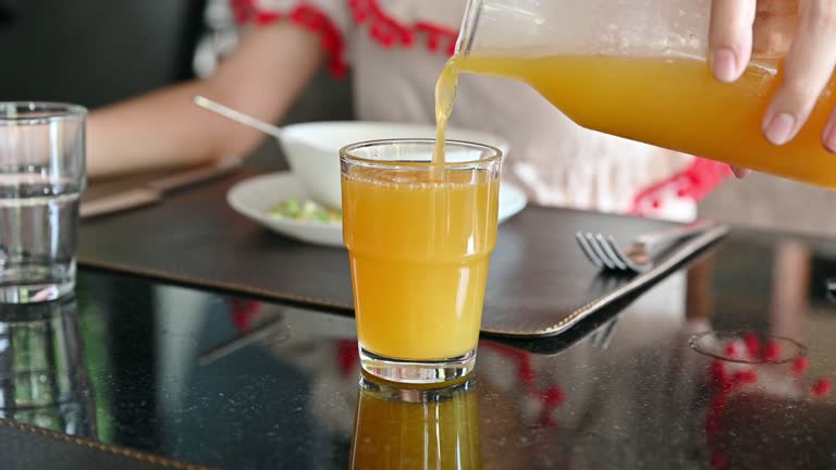 Hand of woman pouring orange juice in the glass on the table