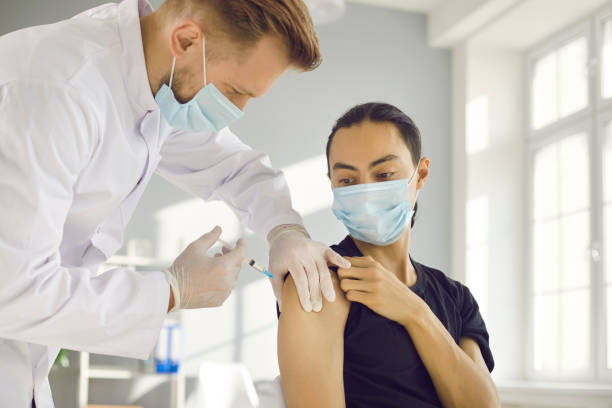 istock Young guy in face mask getting vaccine during immunization campaign at health center 1318650175