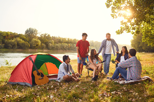 A group of friends have a picnic in a forest near a lake in the summer in autumn.