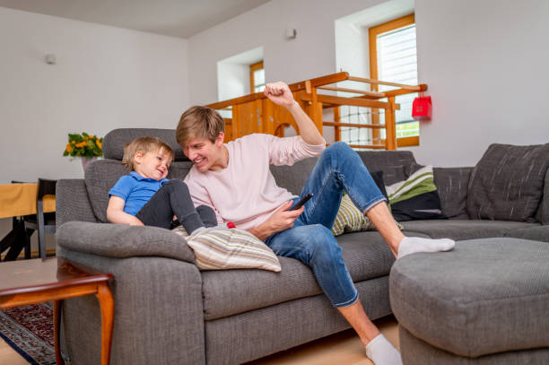 istock Young man and cute little boy sitting on a sofa and watching tv 1318651278