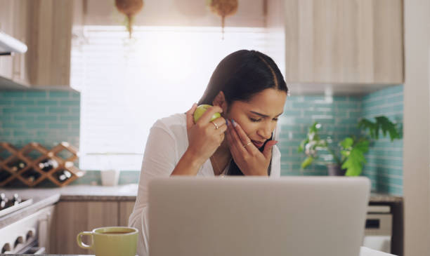 Shot of a young businesswoman suffering from a tooth ache while eating an apple at home I must have bitten down too hard toothache stock pictures, royalty-free photos & images