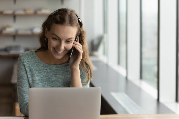 istock Smiling female employee work on laptop talk on cellphone 1318655039