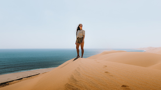 Young woman traveling in Namibia, walking at the big dunes meeting the ocean at Namib-Naukluft National Park