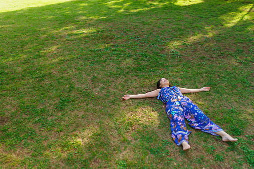 A young woman is lying down on grass and relaxing in nature. Earthing or grounding concept.