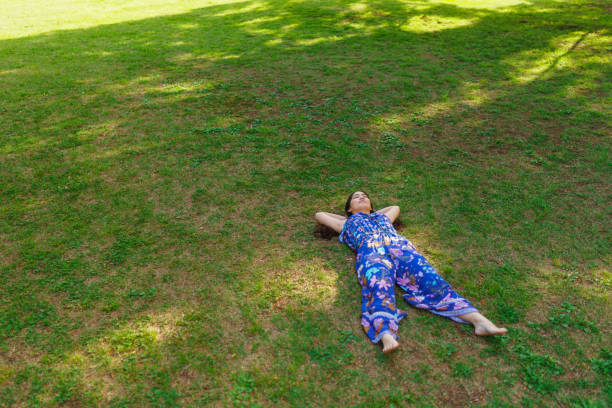 A young woman is lying down on grass and relaxing in nature. Earthing or grounding concept.