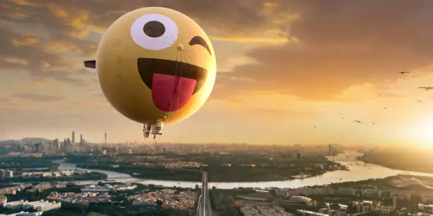 Photo of A Spherical Yellow Airship Or Blimp With A Smiling Emoticon Face In The Dawn Sky Flying Over A City