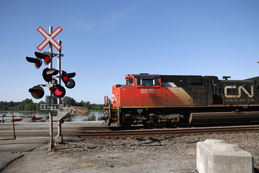 Maple Ridge, Canada - May 16, 2021: Red warning lights flash as CN 8810 heads east at the 225th Street level crossing in Maple Ridge. Background shows the Fraser River flowing through Metro Vancouver in springtime.