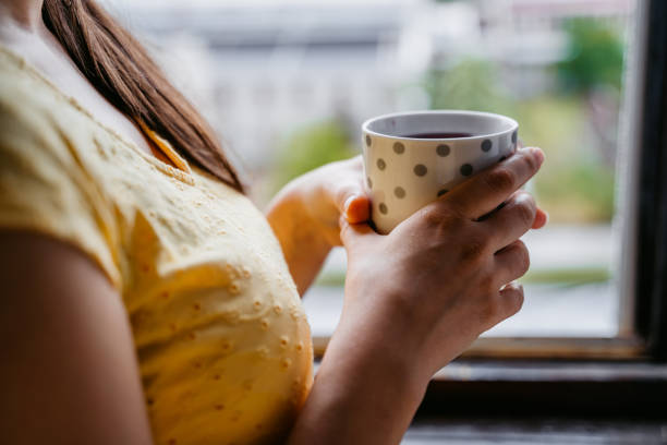 istock Woman holding coffee cup at window 1318665075