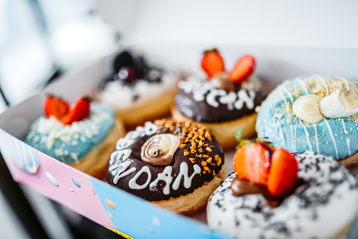 A top down view of a dozen assorted donuts in a box, in a restaurant or kitchen setting.